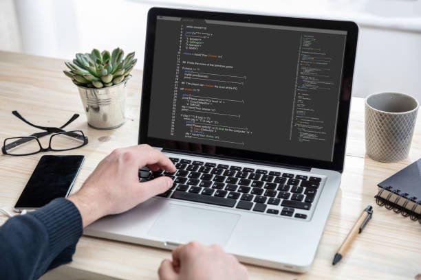 Computer code, software concept. Programmer working with a laptop, programming code on the screen, office background. Developing coding technologies.